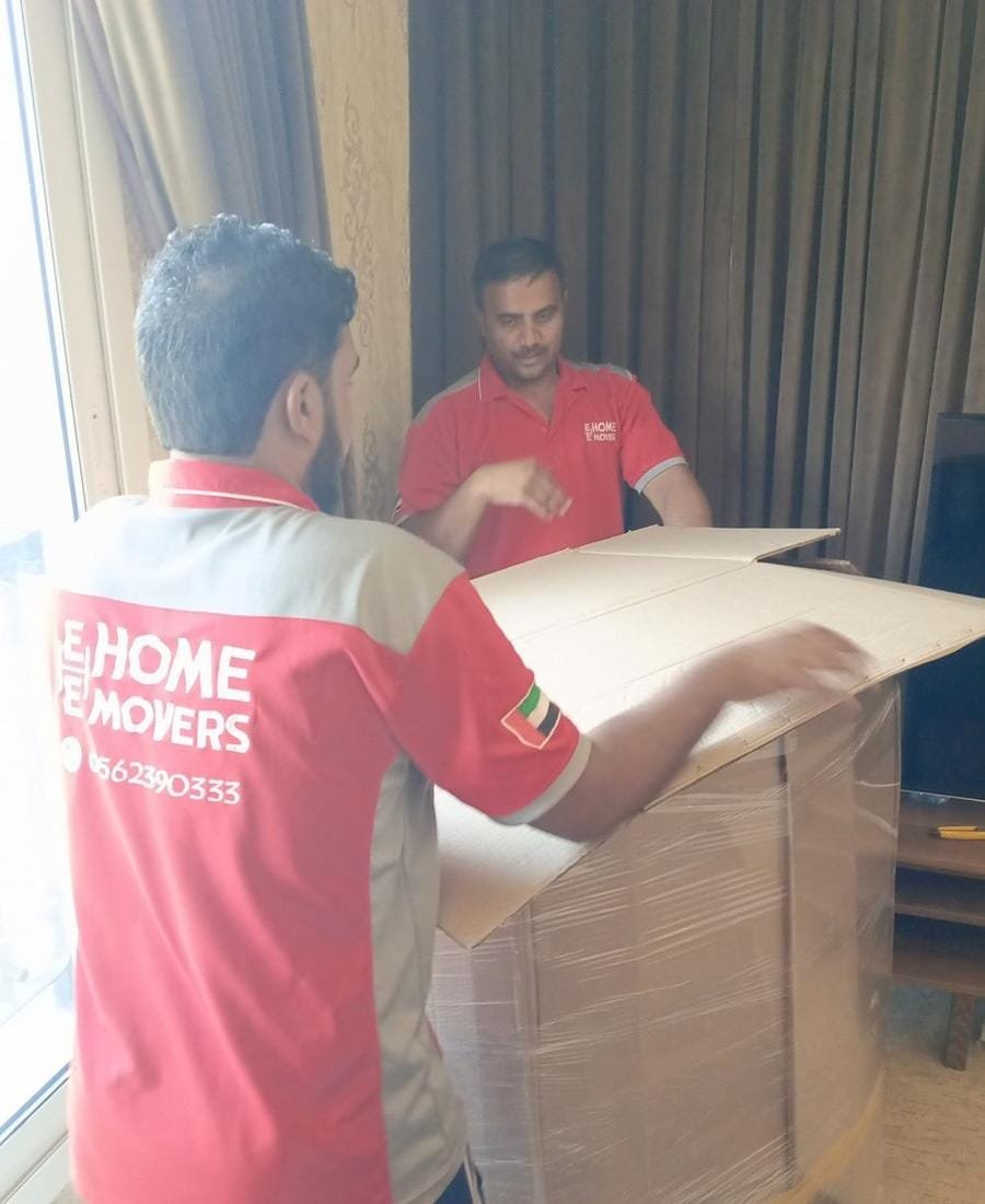 E Home Movers team in red uniforms packing a cardboard carton